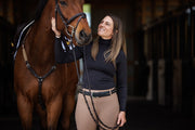 Woman equestrian wearing a black GG turtleneck with built in earbud pockets and cord keepers looking at her horse with love