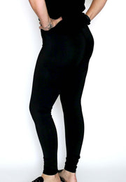 Woman in front of white seamless background standing with her back to the camera, wearing black equestrian workout leggings with slide shoes. Her hands are on her hips.